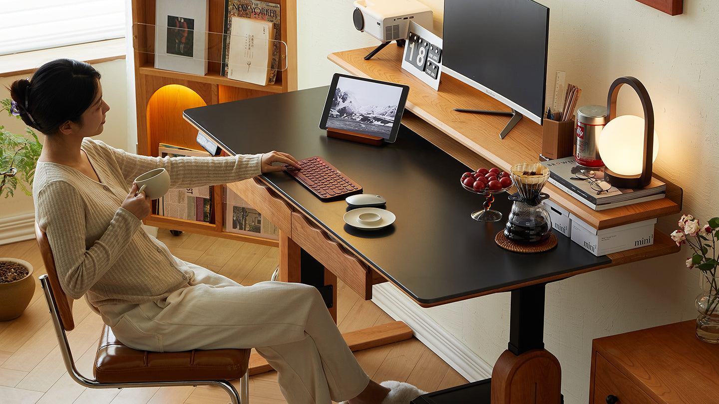Woman enjoying coffee while working at an ergonomic wooden desk, showcasing a cozy workspace for earning Loft Points with purchases at LoftHome